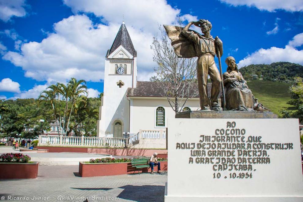Imagem de uma escultura e da igreja no centro de Domingos Martins.